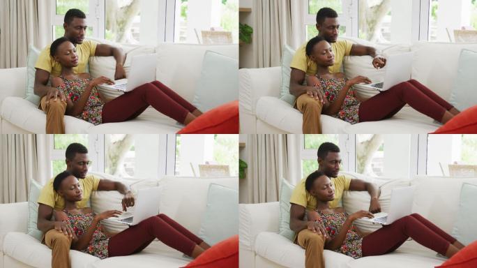 幸福的非裔美国人夫妇在沙发上拥抱和交谈看着笔记本电脑