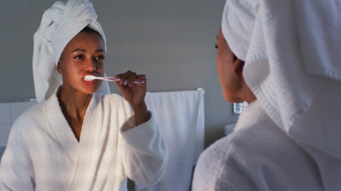 一个穿着浴袍的非洲裔美国妇女在浴室里对着镜子刷牙