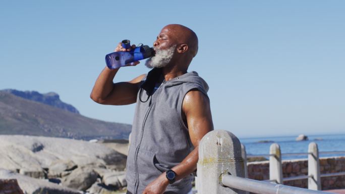 资深非洲裔美国人在海边的岩石上锻炼喝水