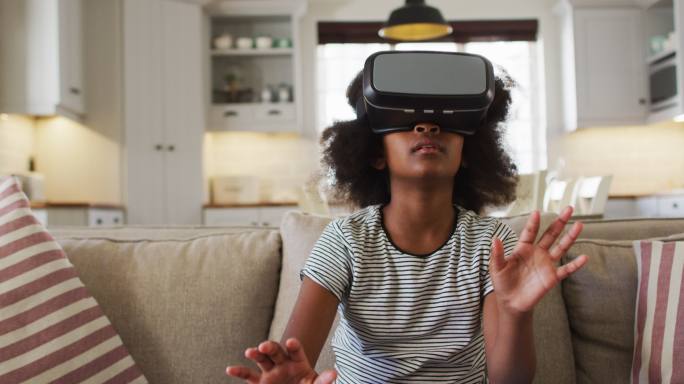 非裔美国女孩坐在沙发上，戴着虚拟现实头盔