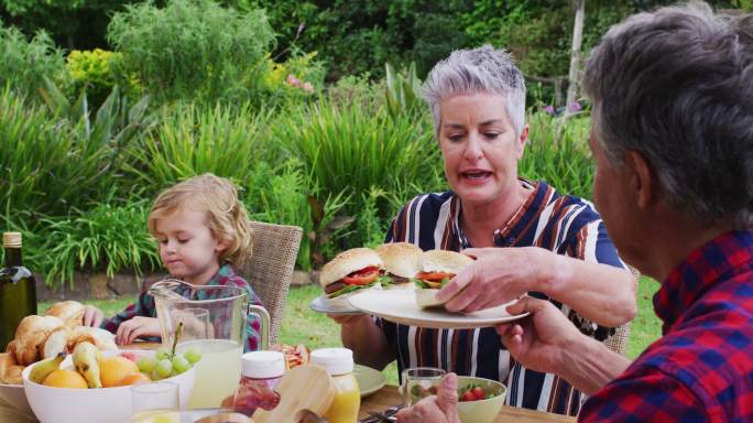 微笑的白人高级妇女服务家庭一起在花园庆祝餐