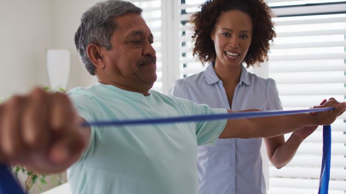 混合种族的女性物理治疗师帮助高级男子使用锻炼带锻炼