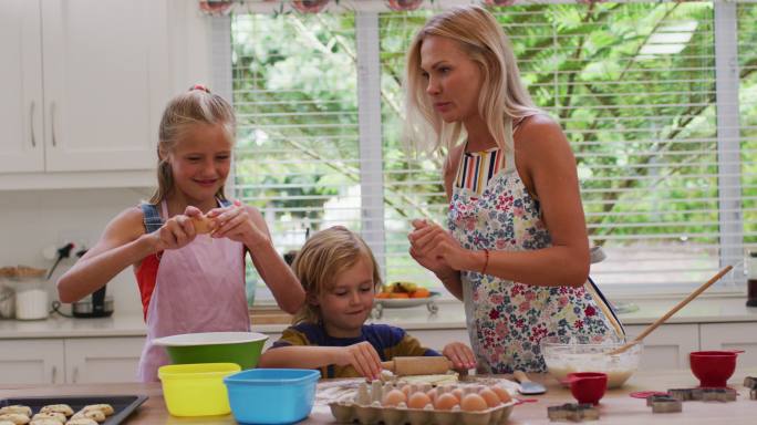 幸福的白人母亲在厨房里与女儿和儿子，穿着围裙一起烤饼干