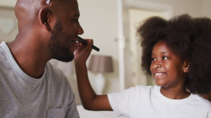 非裔美国女孩在家给戴着皇冠的父亲化妆