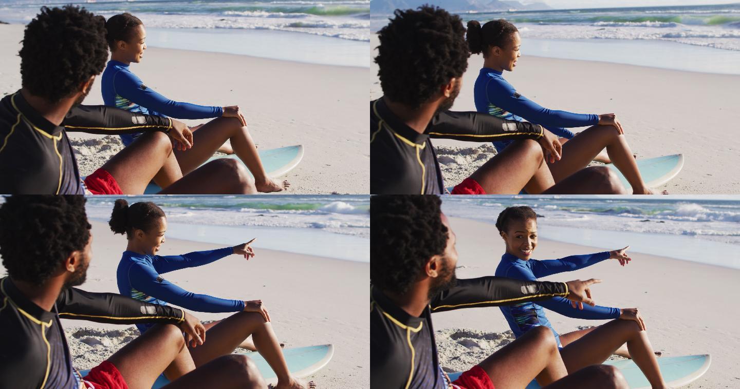 一对非洲裔美国夫妇在海滩上聊天，坐在冲浪板上
