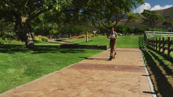 一位戴着耳机背着背包在公园里骑摩托车的非裔美国妇女
