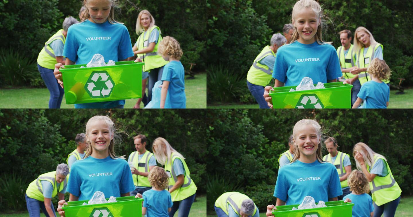 微笑的白人女孩拿着回收盒捡垃圾与志愿者在野外