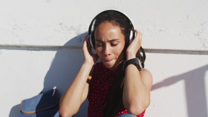 非裔美国妇女戴着耳机，听着音乐在海边散步