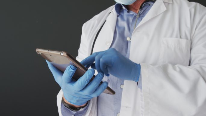 中段白种人男性医生戴着手术手套使用数码平板电脑
