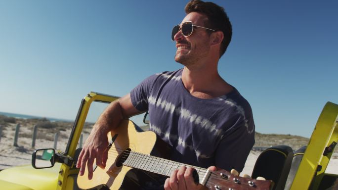 快乐的白人男子坐在沙滩车在海边玩吉它