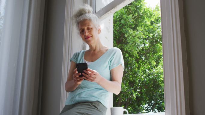 白人老太太在家靠窗边用智能手机