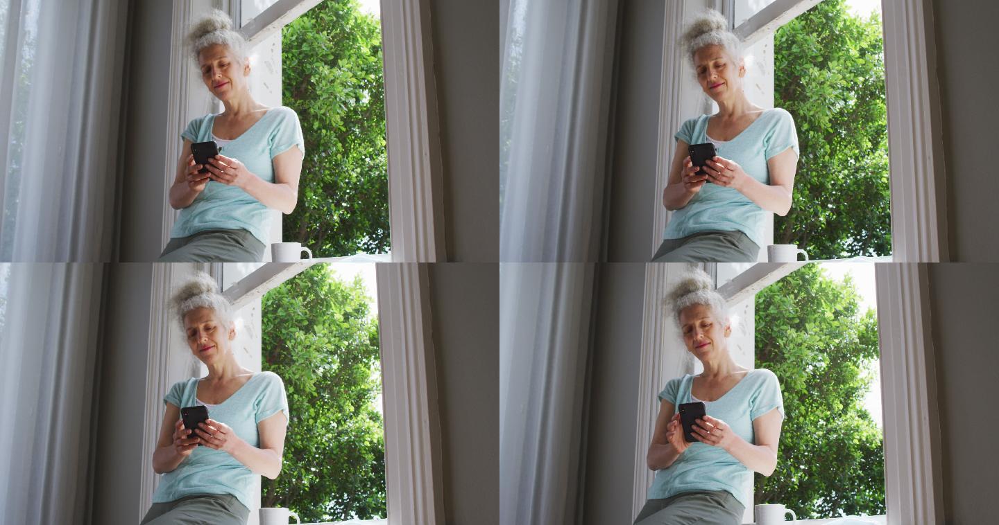 白人老太太在家靠窗边用智能手机