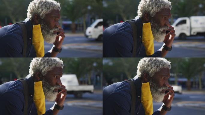 非洲裔美国老人戴着口罩在路上用智能手机讲话的特写