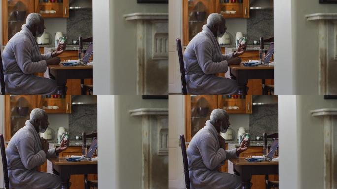 一位非洲裔美国老人拿着空的药物，同时在家里的笔记本电脑上进行视频通话
