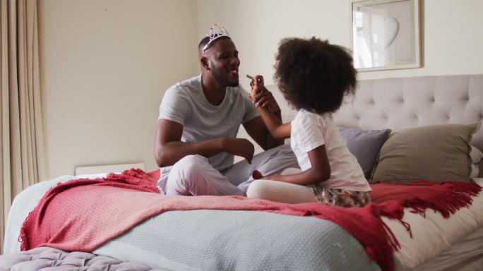 非洲裔美国女孩给她的父亲涂口红，父亲在家里戴着皇冠