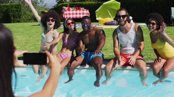 一群不同的朋友坐在泳池边摆姿势拍照