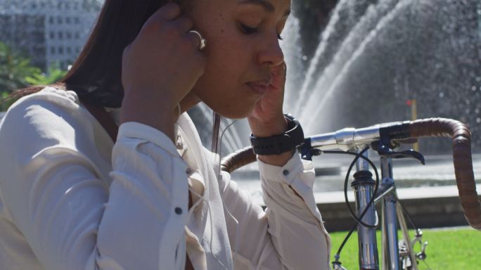 非裔美国妇女骑自行车戴耳机在城市公园