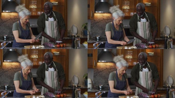 生病的混血老年夫妇穿着围裙在家里的厨房里一起切菜