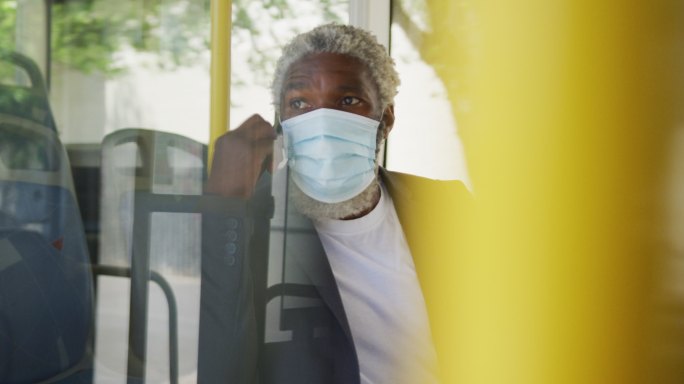 非裔美国老人戴着口罩坐在公交车上用智能手机聊天