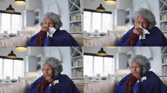 生病的高级非洲裔美国妇女盖着毯子坐在家里的沙发上