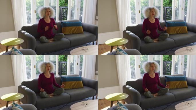 年长的白人妇女坐在家里的沙发上练习瑜伽