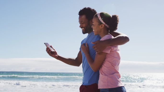 一对非洲裔美国夫妇在海滩上用智能手机微笑自拍