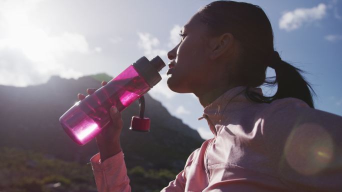 一位非洲裔美国妇女在山里徒步时喝瓶子里的水