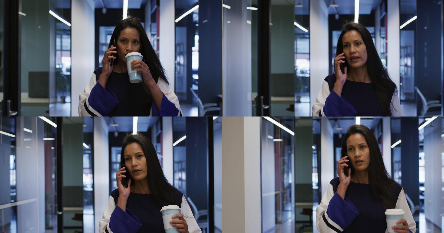 混血女商人拿着咖啡在办公室走廊边走边用智能手机聊天