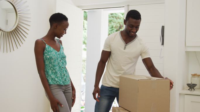 快乐的非裔美国夫妇在屋里整理包装盒，拥抱在一起
