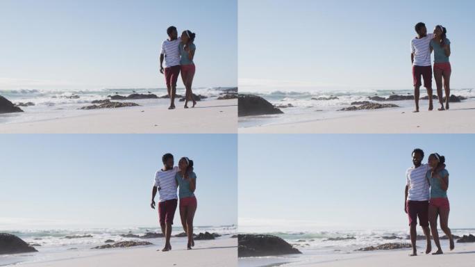 一对非裔美国夫妇微笑着，拥抱着，在海滩上散步