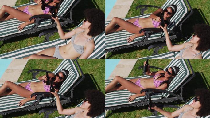 两个混血女性朋友坐在日光浴床上喝啤酒