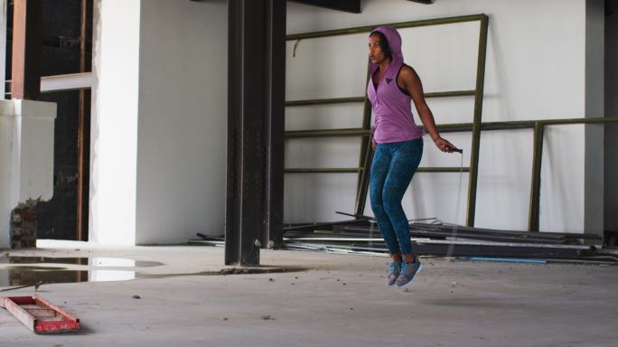 非裔美国妇女穿着连帽衫在空旷的城市建筑里跳绳