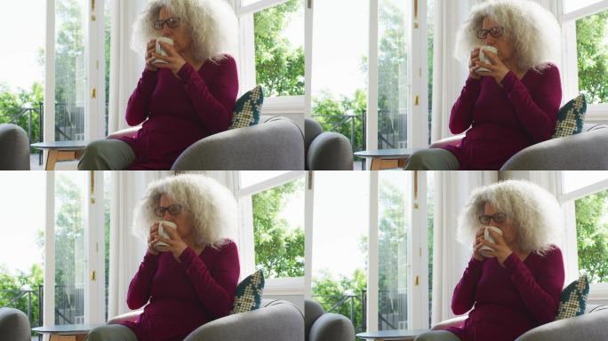 年长的白人女人坐在家里的沙发上喝咖啡