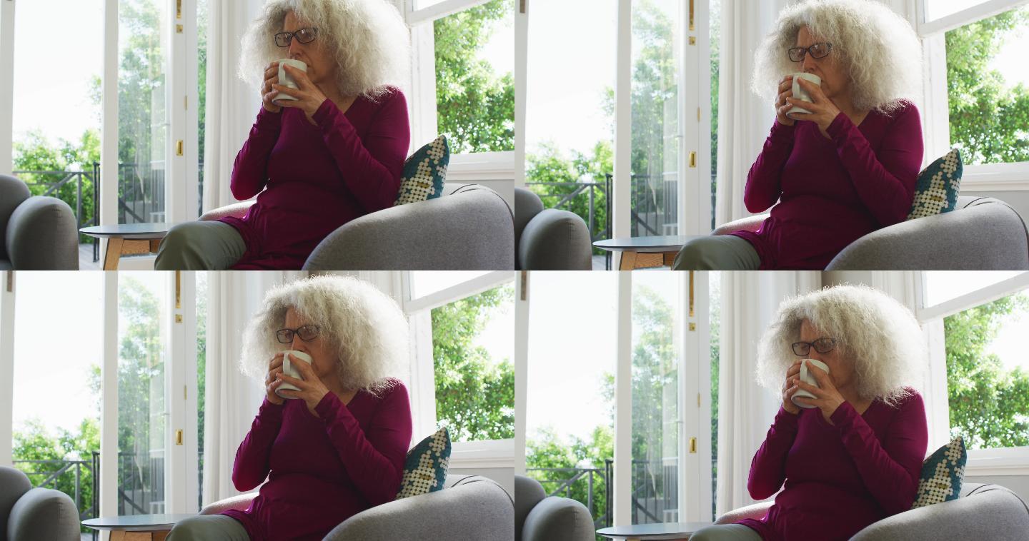 年长的白人女人坐在家里的沙发上喝咖啡