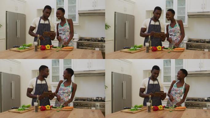 微笑的非洲裔美国夫妇穿着围裙在厨房用药片准备食物