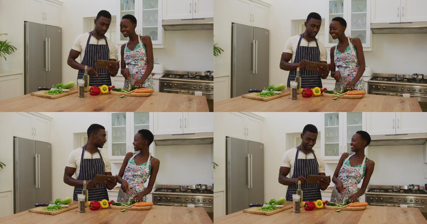 微笑的非洲裔美国夫妇穿着围裙在厨房用药片准备食物