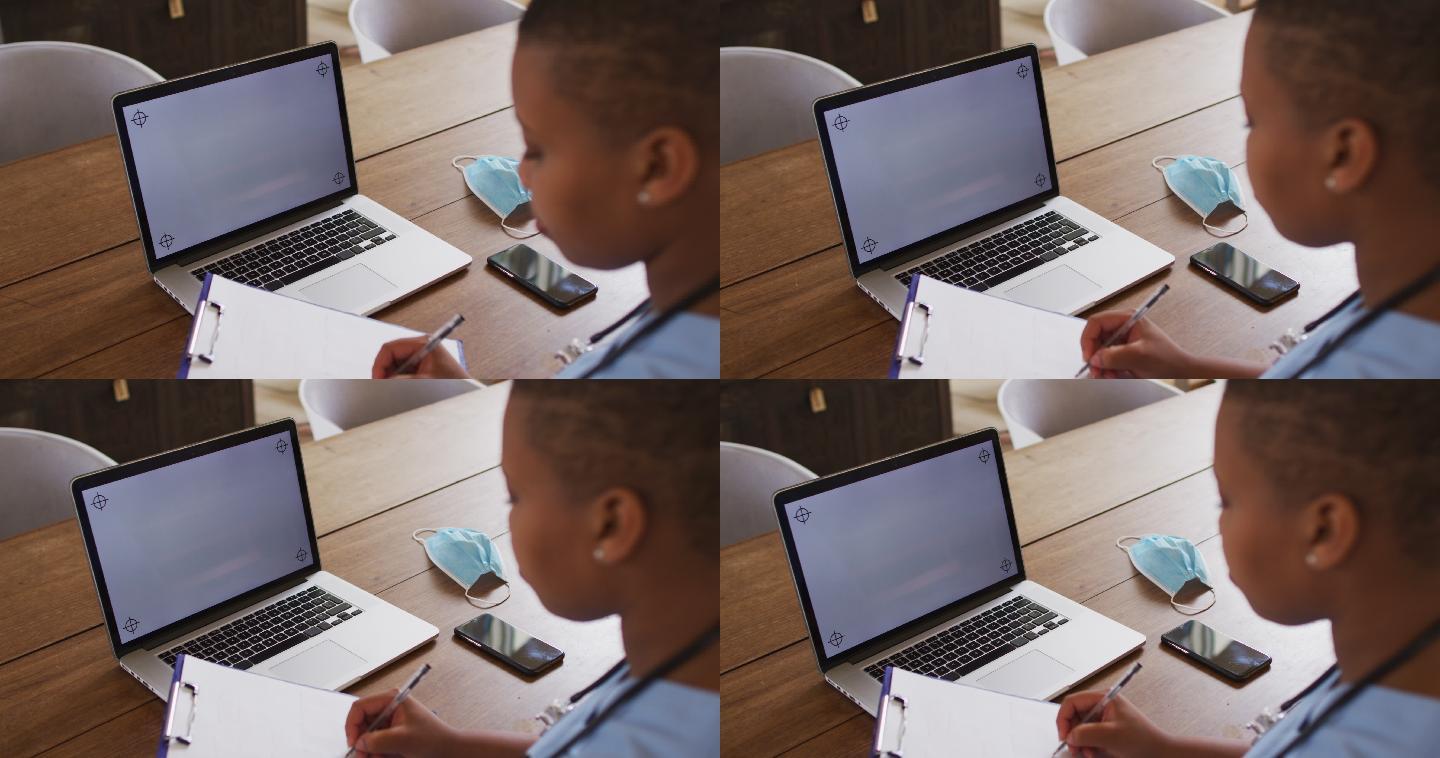 非裔美国女医生在视频通话期间使用笔记本电脑和复制空间做笔记