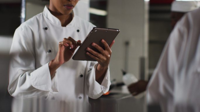 非裔美国女厨师在餐厅厨房使用平板电脑