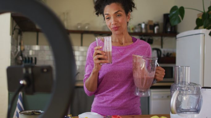 混血女博主在家里的厨房里喝着果汁，用智能手机录音