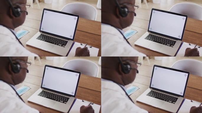 非裔美国男性医生进行视频咨询，头戴耳机，使用笔记本电脑与复制空间