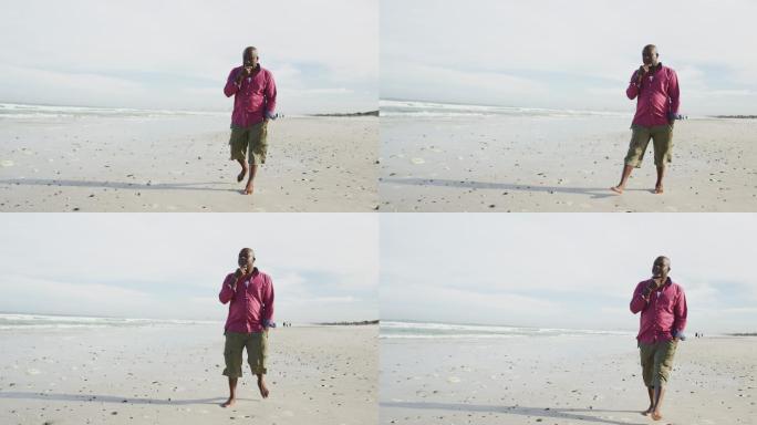 非裔美国老人在沙滩上走着，揉着下巴，看着大海