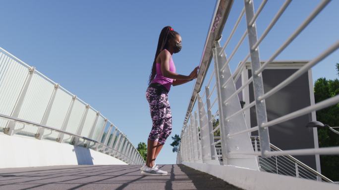一名非裔美国妇女，扶着城市大桥的栏杆伸腿