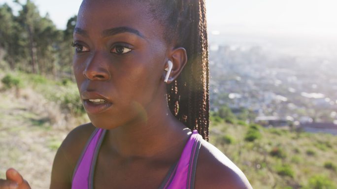 一名非洲裔美国妇女在日落时分戴着无线耳机在户外运动