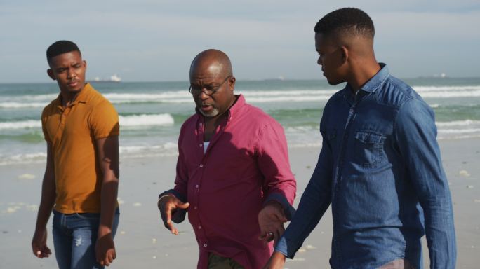 一位非洲裔美国老人和一对十几岁的儿子在海滩上散步聊天