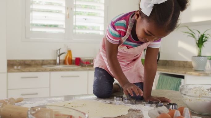 快乐的非洲裔美国女孩在厨房里用切饼干的刀