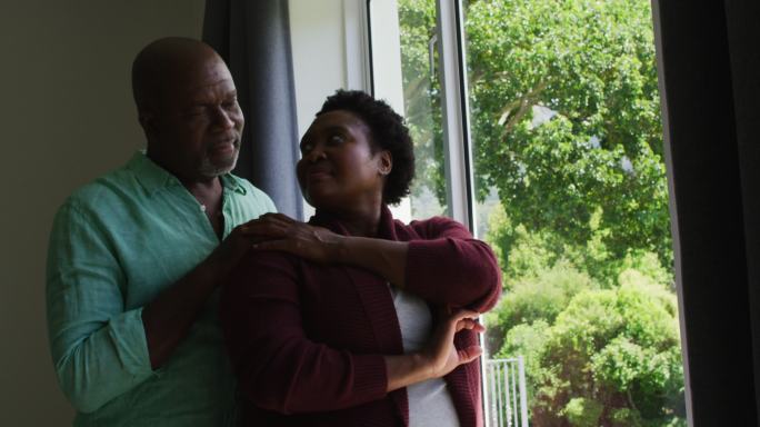 非裔美国老人夫妇在家中看着窗外互相拥抱