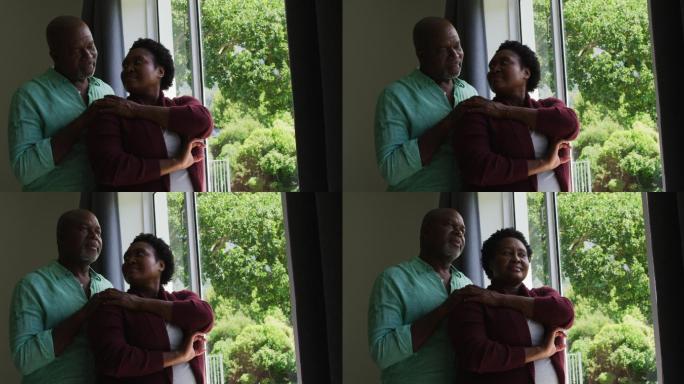 非裔美国老人夫妇在家中看着窗外互相拥抱
