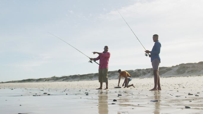 一位非洲裔美国老人和两个十几岁的儿子站在海滩上钓鱼聊天