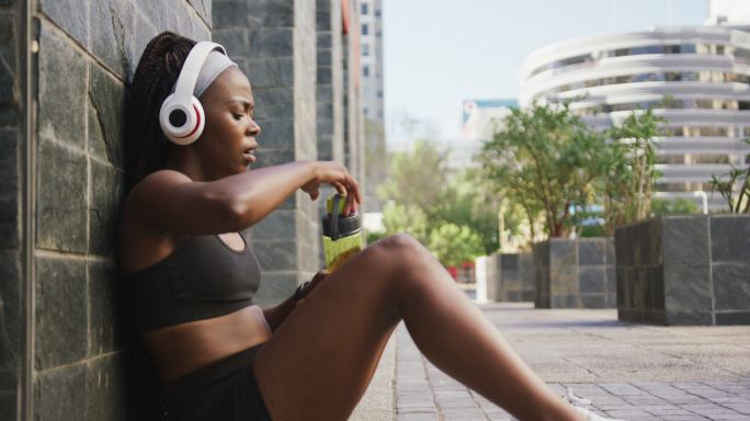 非裔美国妇女在户外运动，戴着无线耳机在城市饮水