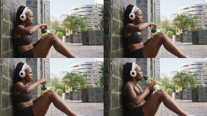非裔美国妇女在户外运动，戴着无线耳机在城市饮水